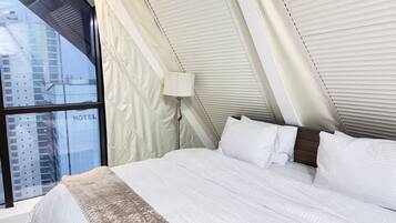 A hotel room with a large window, a bed with white bedding, and a lamp.