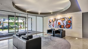A modern lobby with glass doors, a seating area with leather chairs, and a colorful abstract painting on the wall. - The Roy Luxury 3BR with Huge Entertainer's Terrace (Melbourne)