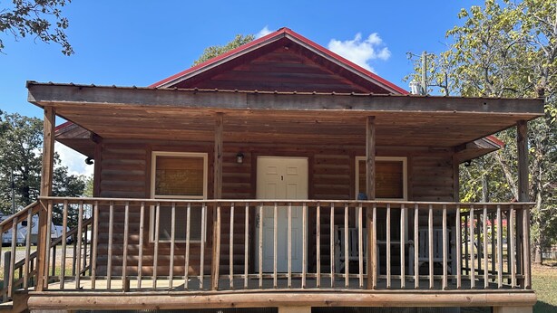 Une cabane en bois avec une véranda, une porte et une fenêtre.
