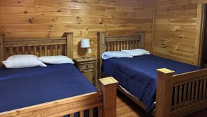 Une chambre dans un chalet en bois, avec deux lits, une table de chevet et un luminaire au plafond.