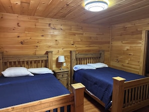 Una habitación de cabaña de madera con dos camas, una mesita de noche y una lámpara de techo.