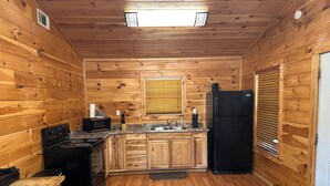 Une cuisine de taille réduite avec des murs en bois, un réfrigérateur noir, une cuisinière et un four à micro-ondes.