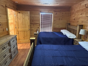 A wooden room with two beds, a dresser, and a window with blinds.