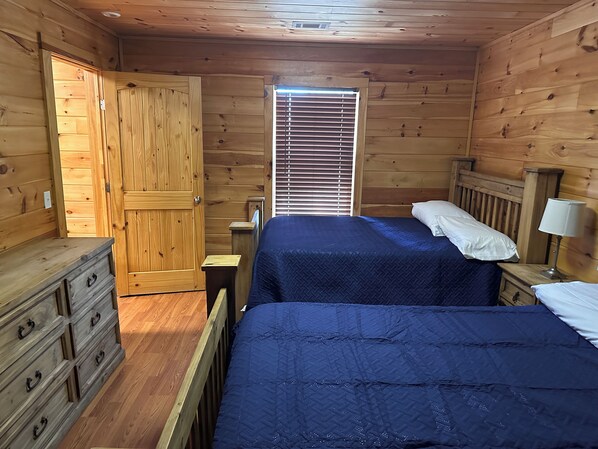A wooden room with two beds, a dresser, and a window with blinds.