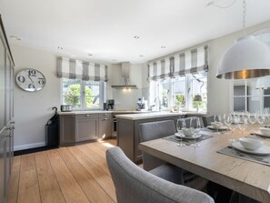 A modern kitchen with a dining area, featuring a large island, ample natural light, and a clock on the wall. - Holiday Home With 4 Bedrooms (Sylt)