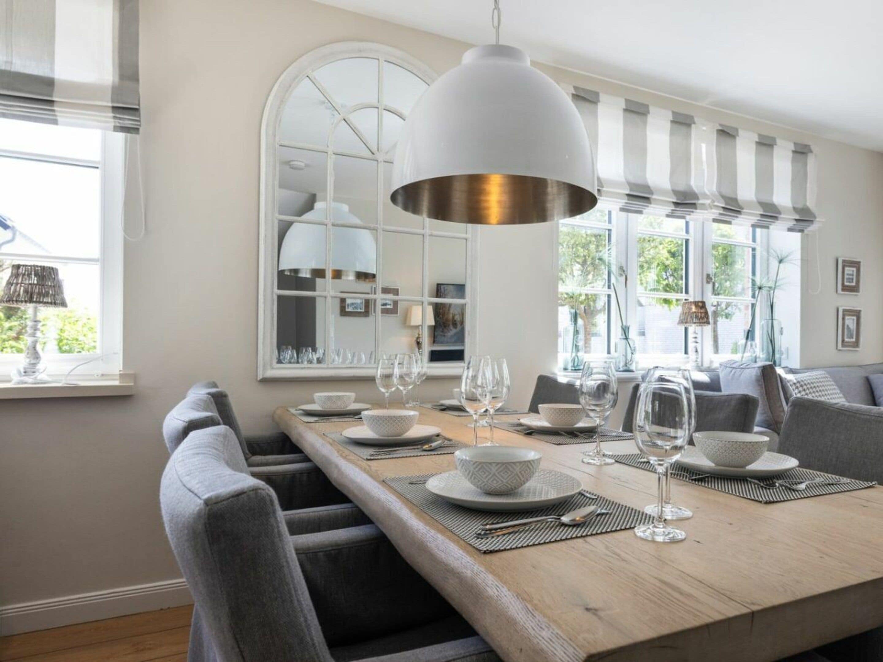 A dining area with a long wooden table, grey upholstered chairs, and a large white pendant light.