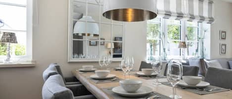 A dining area with a long wooden table, grey upholstered chairs, and a large white pendant light.