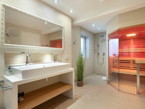 A modern bathroom with a large mirror, a white sink, a shower area, and a glass-enclosed sauna. - Holiday Home With 4 Bedrooms (Sylt)