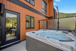 A hot tub on a balcony with a wooden exterior wall and a door leading to a patio area. - Montane | Slope-Side | Hot Tub | Resort Access (Panorama)