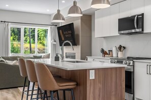 A modern kitchen with a central island, bar stools, a built-in microwave, and a large window offering a view of greenery.