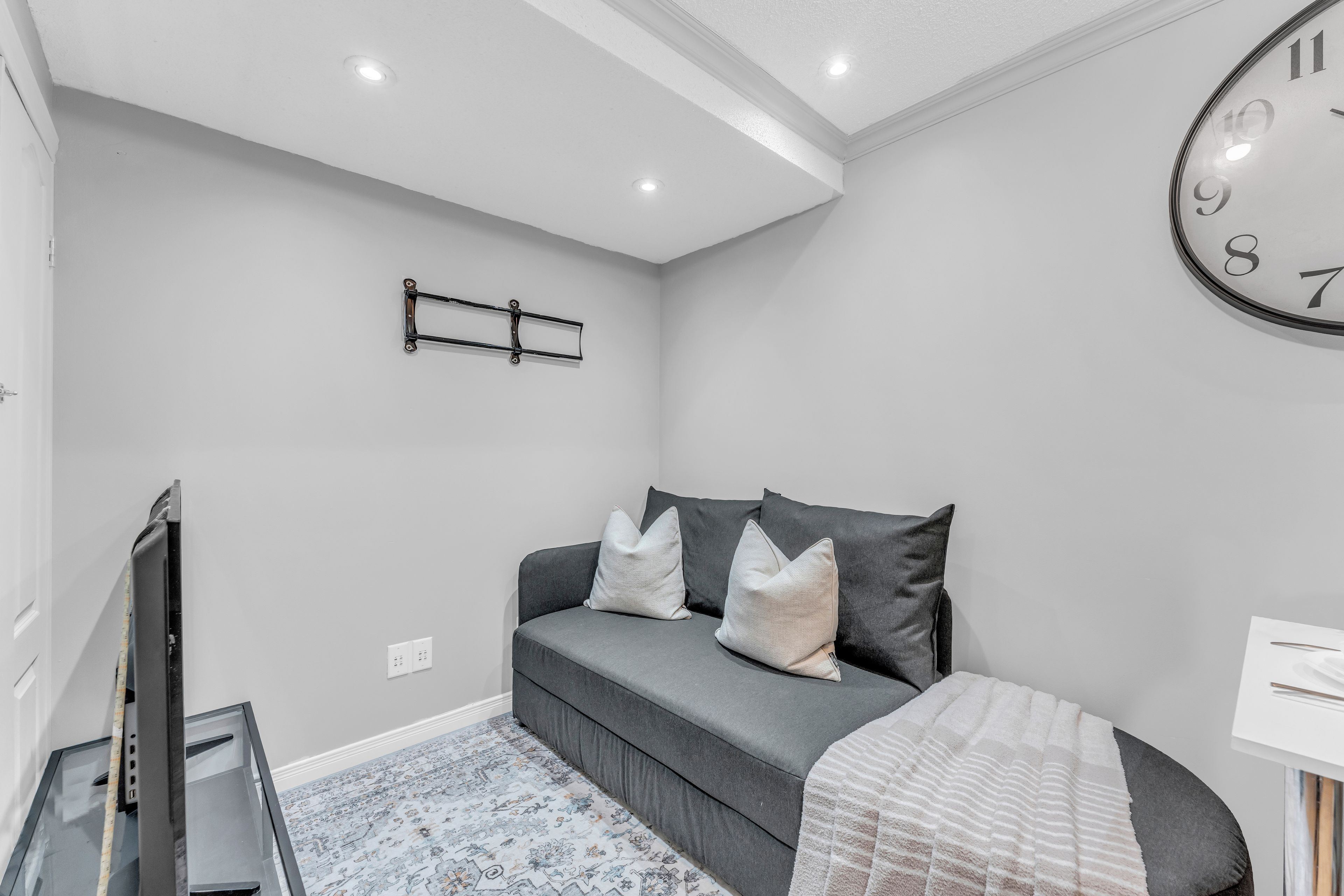 A modern bedroom with a grey sofa, a large wall clock, and a flat-screen TV.