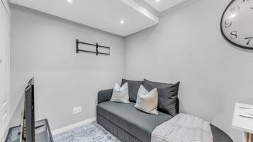 A modern bedroom with a grey sofa, a large wall clock, and a flat-screen TV.