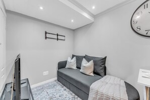 A modern bedroom with a grey sofa, a large wall clock, and a flat-screen TV.