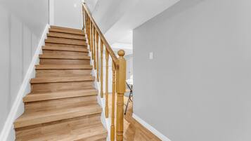 A wooden staircase with a handrail, white walls, and a wooden floor.