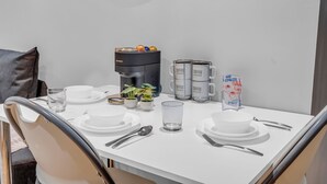 Siisti ruokapöytä, jonka päällä on valkoisia lautasia, aterimia ja kahvinkeitin.