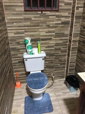 Ein kleines Badezimmer mit Toilette, einer blauen Matte, einem Pömpel und einem Mülleimer.