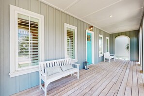 A covered porch with a wooden floor, white benches, and a turquoise door. - Palmilla Beach Resort-142 Sunset Avenue (Port Aransas)