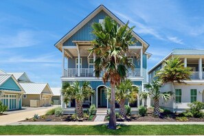 A two-story house with a balcony, surrounded by palm trees and a well-maintained lawn. - Palmilla Beach Resort-142 Sunset Avenue (Port Aransas)