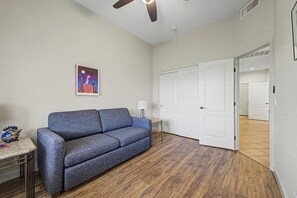 A room with a blue sofa, a small table, a lamp, and a door leading to another room. - Southwest 3 bed 2 bath Home w/Patio/BBQ/Pool/Spa (Fountain Hills)
