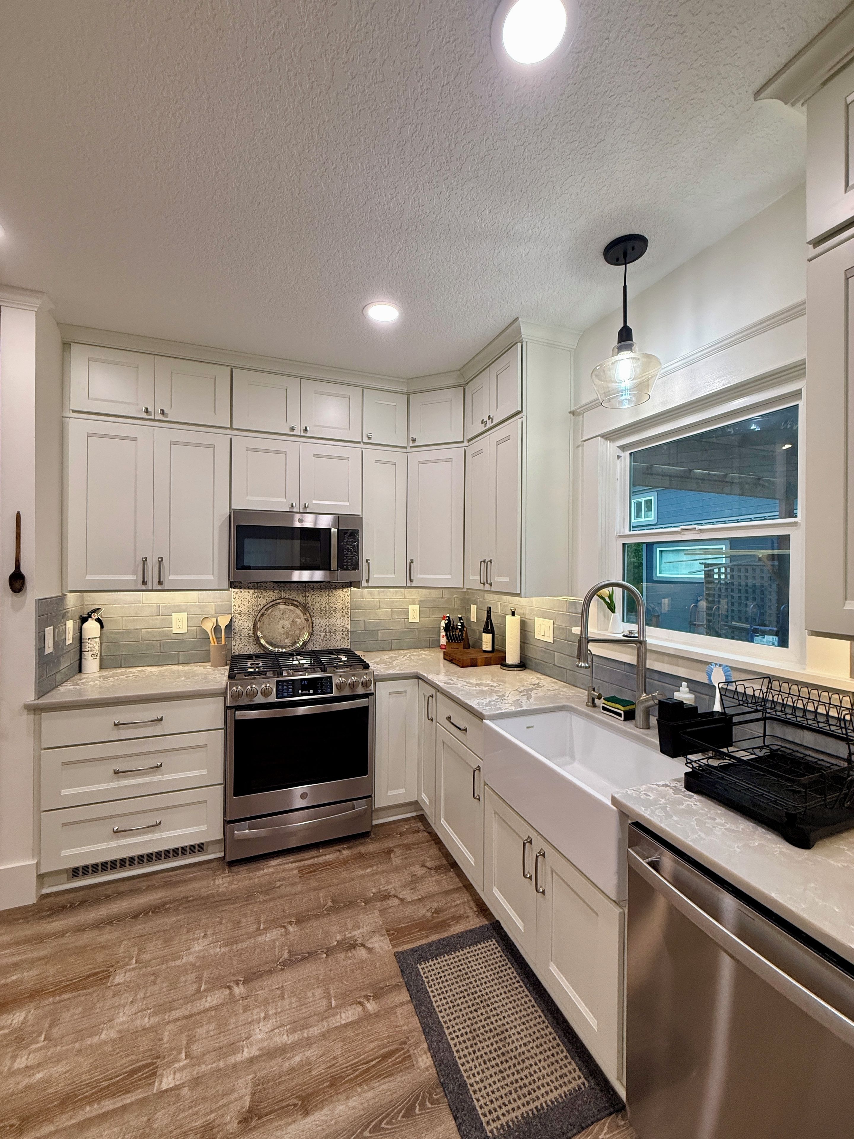 Una cocina con armarios blancos, electrodomésticos de acero inoxidable, microondas y ventana con vistas.