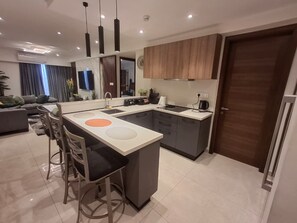 A modern kitchen with a central island, bar stools, a built-in oven, and a large mirror above the island. - Cozy 1-bedroom executive apartment in beautiful Accra with AC and gym (Accra)