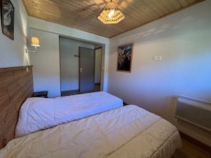Ein Schlafzimmer mit Holzbalkendecke, einem Bett mit weißer Bettwäsche, einer Wandleuchte und einer Tür zu einem anderen Raum.