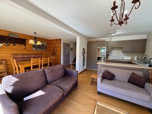 A modern living room with a wooden dining area, a kitchen with stainless steel appliances, and a staircase leading to another level. - Duplex 8 pers - Vue montagne - Balcon sud - Pistes à 100 m (Vars)