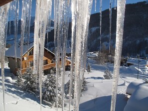 Eine Holzhütte vor einer verschneiten Landschaft, mit Eiszapfen, die vom Dach hängen.