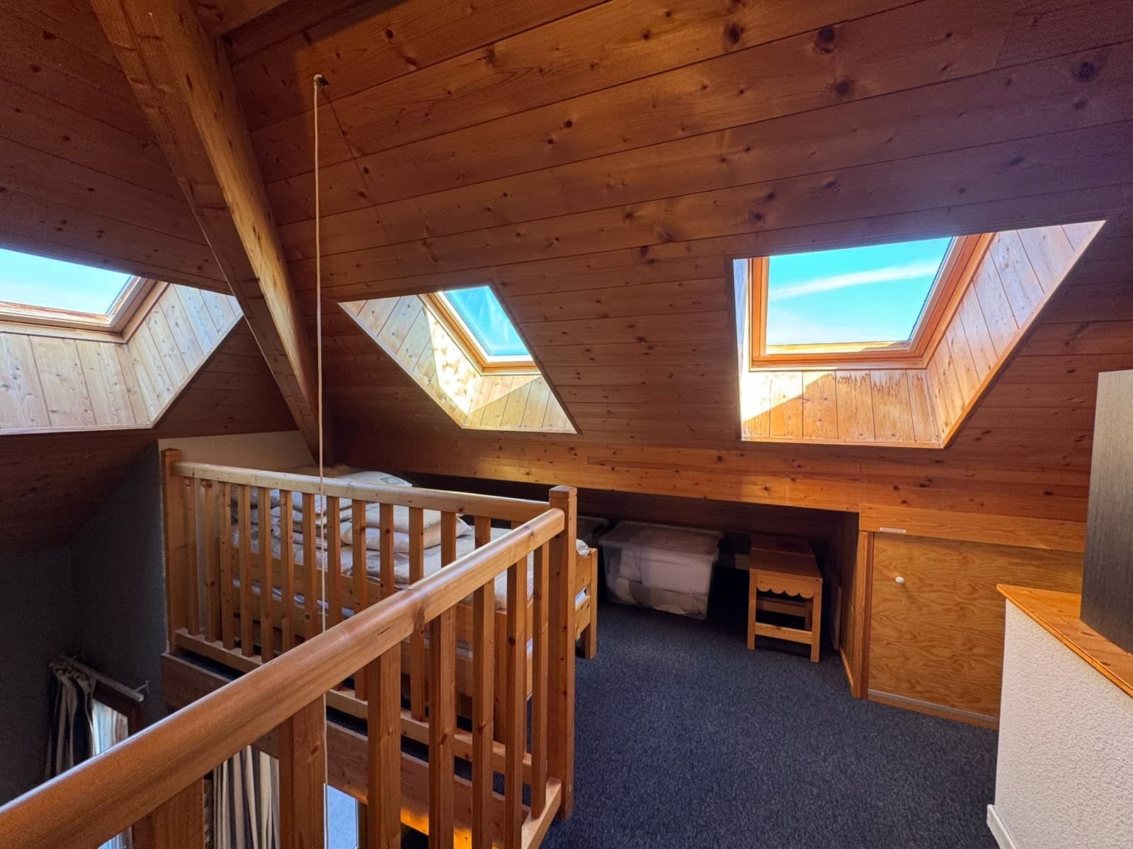 Ein Holzinnenraum mit Dachfenstern, einer Treppe und einem kleinen Bett.