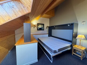 Ein kleines Zimmer mit einem Bett, einem Nachttisch und einer Wandlampe.