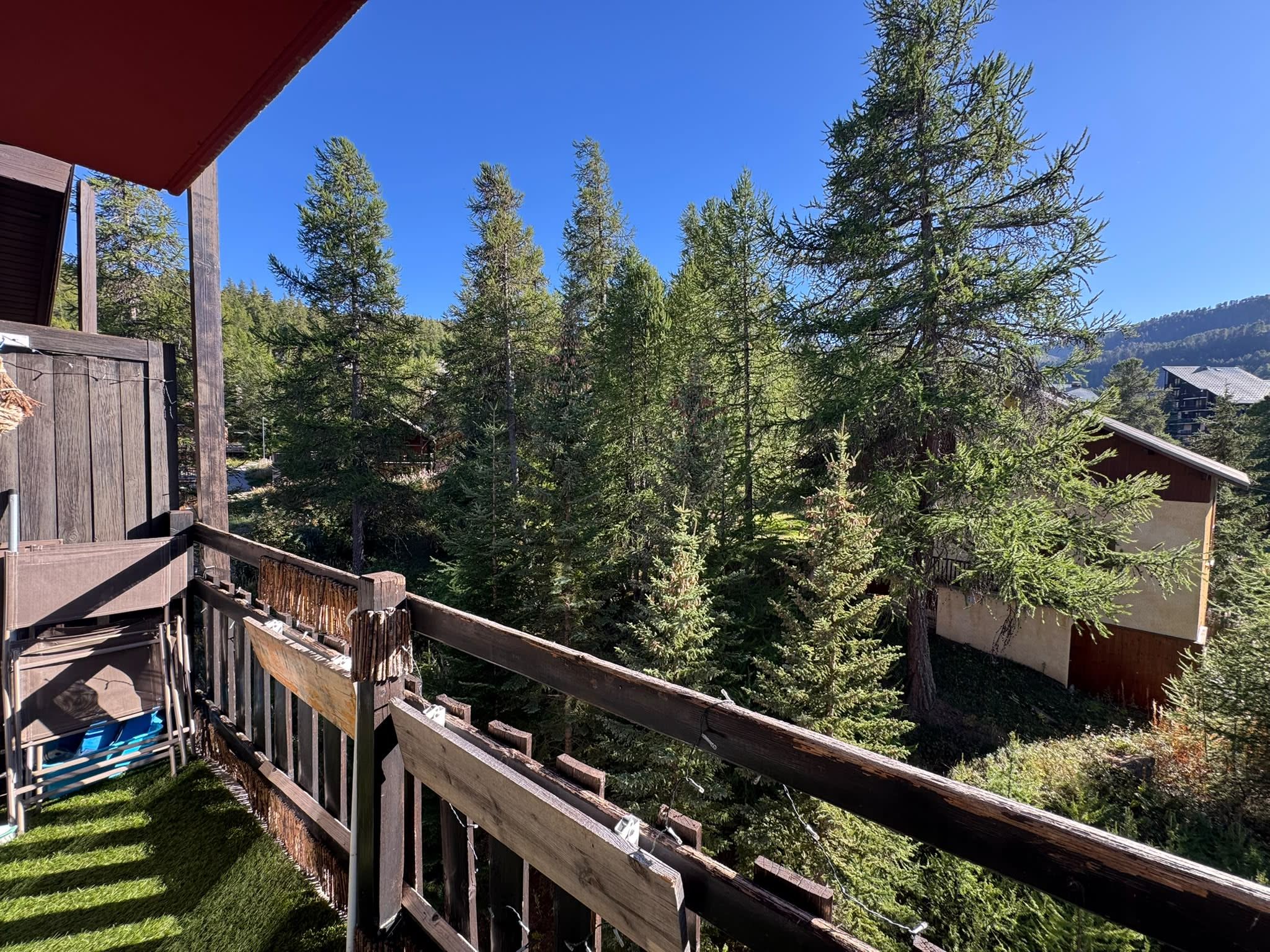 A wooden deck with a view of a forested area and a building in the background.
