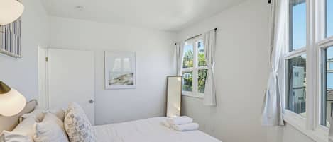 A bedroom with a bed, a bedside lamp, a window, and a door.