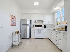 Cozinha moderna com armários brancos, eletrodomésticos de aço inoxidável e piso ladrilhado.