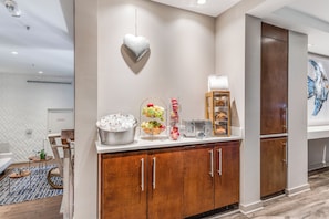 Een hotelkamer met kitchenette, een lamp in de vorm van een hart, een schaal fruit en een schilderij aan de muur.