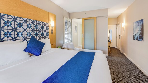 A hotel room with a large bed, a patterned headboard, a blue throw, and a hallway leading to a bathroom. - The Landon Bay Harbor (Bay Harbor Island)