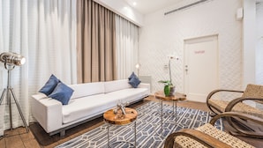 A modern living room with a white sofa, a coffee table, and a lamp. There is a door with a fire alarm panel sign. - The Landon Bay Harbor (Bay Harbor Island)