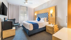 A hotel room with a bed, bedside table, chair, TV, and a window with curtains. - The Landon Bay Harbor (Bay Harbor Island)