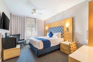 Een hotelkamer met een bed, nachtkastje, stoel, televisie en een raam met gordijnen.