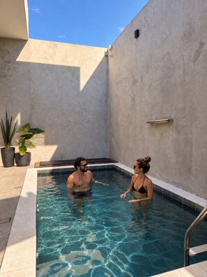 A swimming pool with two people in it, surrounded by a concrete wall and potted plants. - Casa Flora Peruibe • Swimming pool • Arcade games • Check-out at 3 PM (Peruíbe)