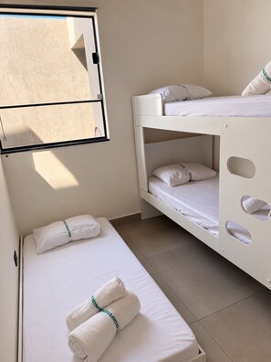 A room with two beds, one with a bunk and one single. There is a window with blinds partially open. - Casa Flora Peruibe • Swimming pool • Arcade games • Check-out at 3 PM (Peruíbe)
