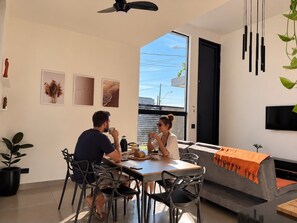 A modern dining area with a table, chairs, and a sofa. There is a television mounted on the wall and a ceiling fan. - Casa Flora Peruibe • Swimming pool • Arcade games • Check-out at 3 PM (Peruíbe)