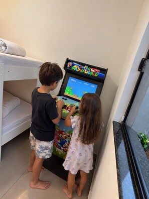 Two children playing a video game on a console in a room with a bunk bed and a window. - Casa Flora Peruibe • Swimming pool • Arcade games • Check-out at 3 PM (Peruíbe)