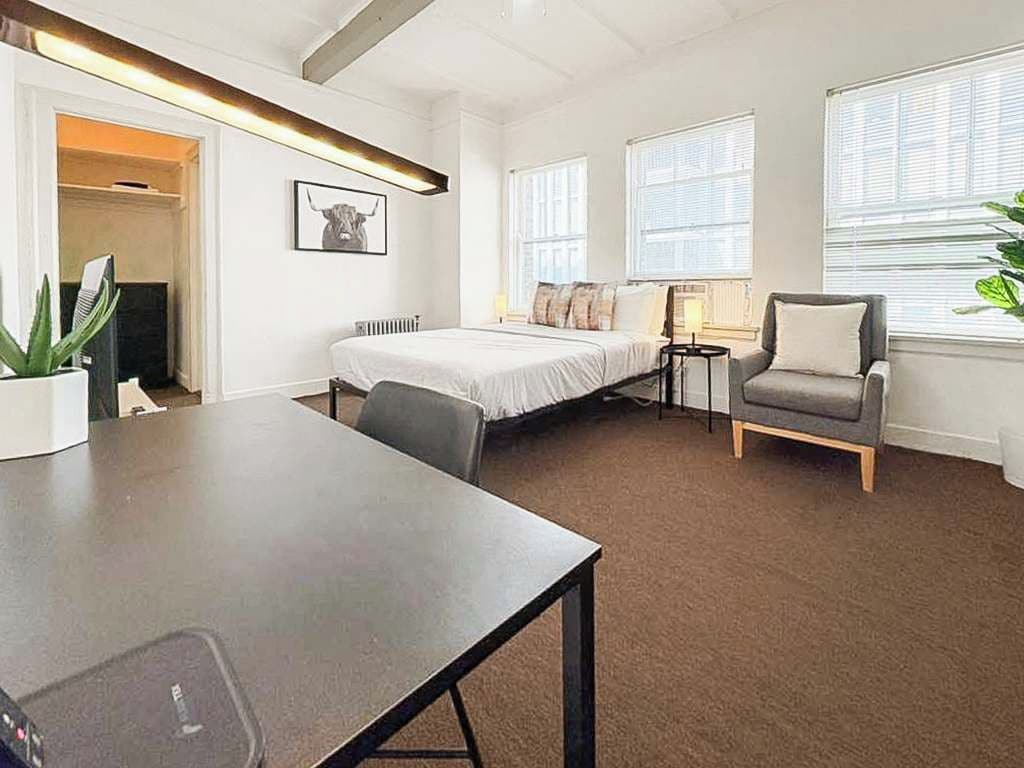 A modern hotel room with a bed, a desk, a chair, and a large window.