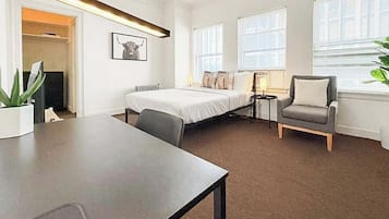 A modern hotel room with a bed, a desk, a chair, and a large window.