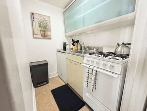 A compact kitchen with a gas stove, a small refrigerator, and a single cabinet. - Trendy Gold Coast Studio Close to Downtown (Chicago)