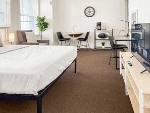 A hotel room with a bed, a desk, two chairs, a coffee machine, a TV, and a clock on the wall. - Trendy Gold Coast Studio Close to Downtown (Chicago)