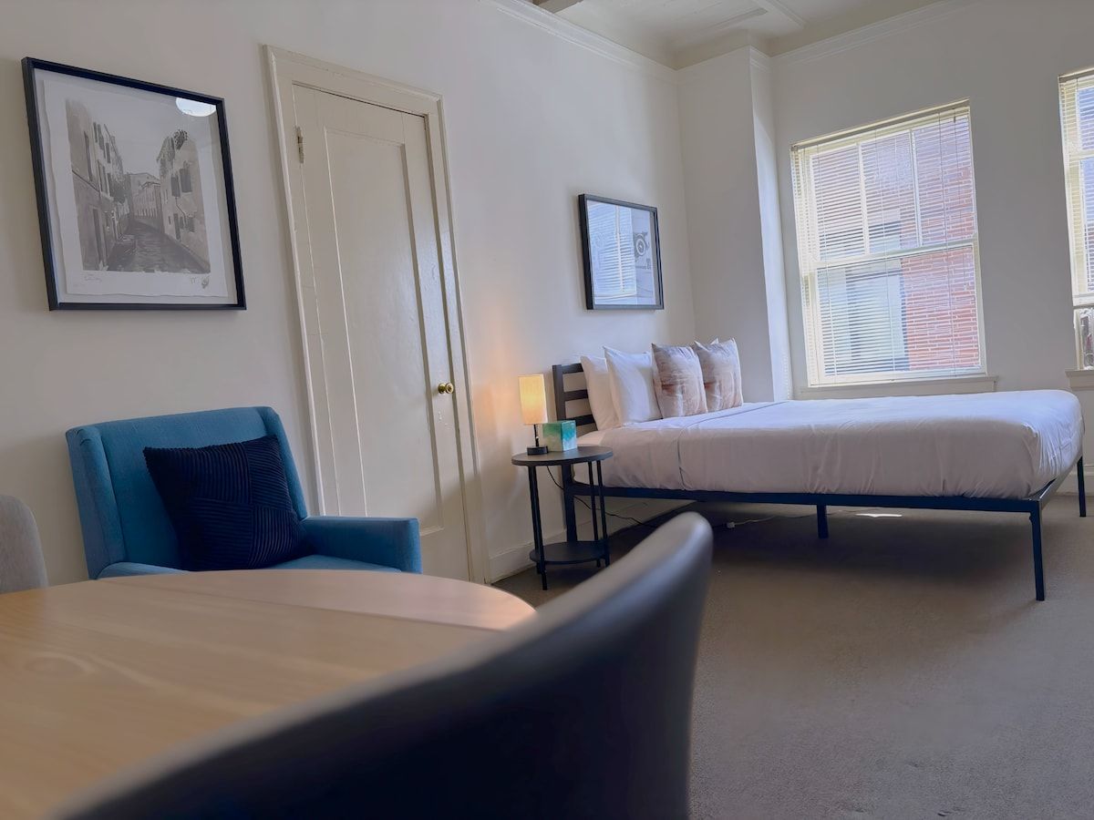 Ein Hotelzimmer mit zwei Betten, einem Sessel, einem Nachttisch mit Lampe und gerahmten Bildern an den Wänden.