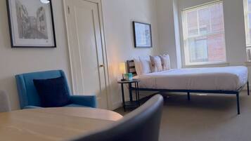 Ein Hotelzimmer mit zwei Betten, einem Sessel, einem Nachttisch mit Lampe und gerahmten Bildern an den Wänden.