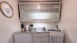 A compact kitchen with a refrigerator, stove, sink, and a framed picture on the wall. - Gold Coast Hideaway | Vintage & Inviting Studio (Chicago)