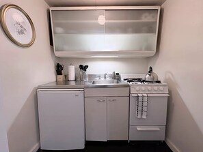 A compact kitchen with a refrigerator, stove, sink, and a framed picture on the wall. - Gold Coast Hideaway | Vintage & Inviting Studio (Chicago)
